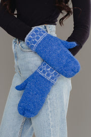 A person, shown from the torso and arms against a gray background, is wearing light blue jeans, a black long-sleeve top, and Blue & Light Blue Patterned Knit Mittens by Panache Apparel Collection.