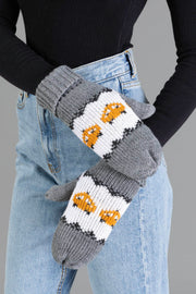 A person wearing light blue jeans and a black long-sleeve shirt stands with their arms crossed. They are wearing Panache Apparel Collection’s gray knit mittens featuring an orange fox pattern.