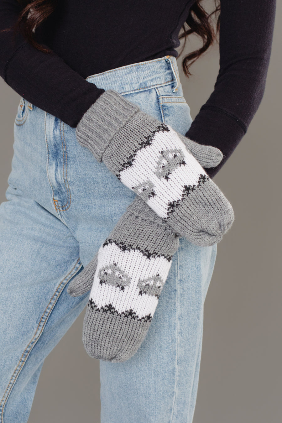 A person wearing light blue jeans and a black long-sleeve shirt, with their arms crossed, displays the Panache Apparel Collection’s Gray with Gray Fox Pattern Knit Mittens.