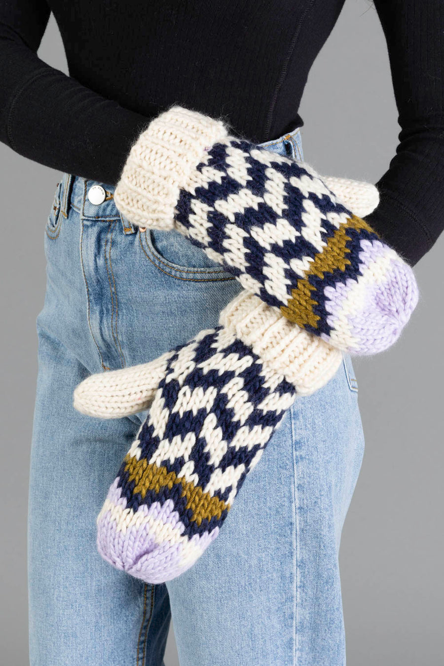 A person wearing light blue jeans, a black top, and a pair of Panache Apparel Collection Beige, Navy & Lilac Patterned Mittens.