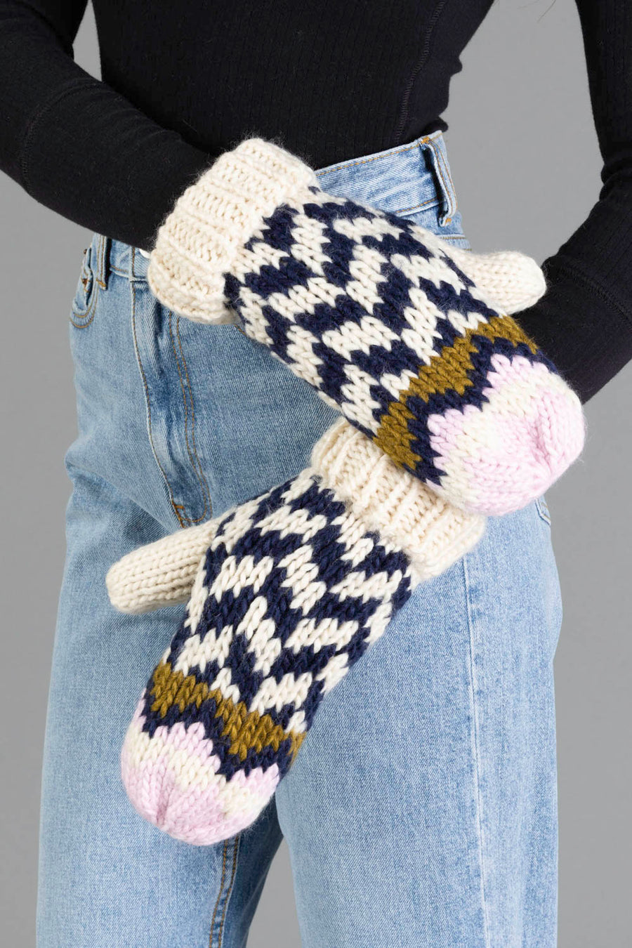 A person wearing high-waisted blue jeans and a black top showcases the Panache Apparel Collection Beige, Navy & Light Pink Patterned Mittens against a plain gray background.