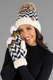 Smiling woman wearing the Panache Apparel Collection Beige, Navy & Light Pink Patterned Pom Hat and matching knit mittens, dressed in a black top and posing in front of a gray background.