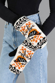 A person in blue jeans and a black top showcases the Panache Apparel Collection Black & Cream Bird Pattern Knit Mittens, featuring bird and orange berry designs on a white background.