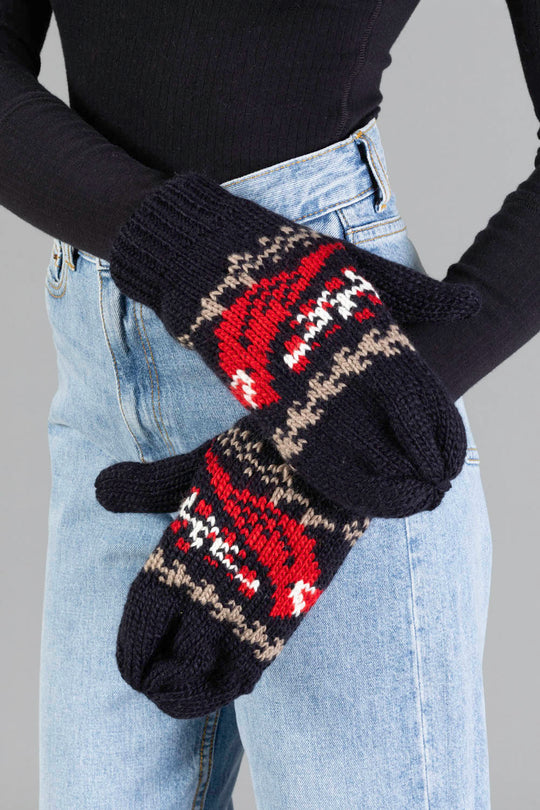 A person wearing blue jeans and a black long-sleeve top holds up the Panache Apparel Collection Black Cardinal Pattern Mittens.