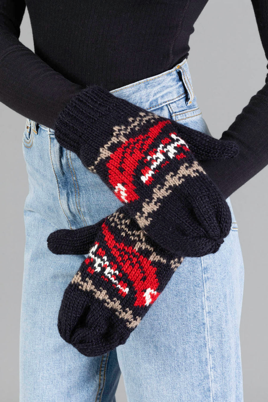 A person wearing blue jeans and a black long-sleeve top holds up the Panache Apparel Collection Black Cardinal Pattern Mittens.