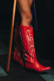 A person wearing Panache Apparel Collection’s Red Embroidered Western Boots stands next to a wooden cane, with a tiled floor visible beneath.