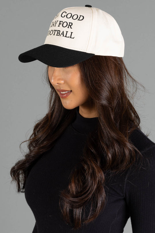 A woman with long brown hair, dressed in a black top, stands against a plain gray background wearing the Panache Apparel Collection’s "It's A Good Day For Football" Two-Toned Trucker Hat.