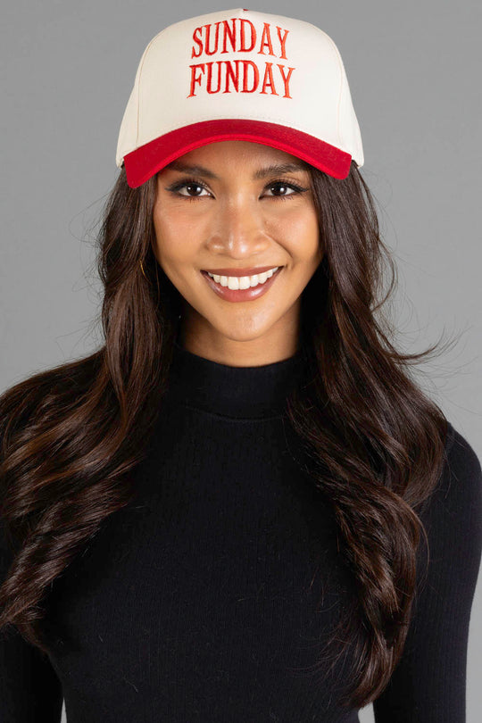A smiling woman with long brown hair and a black top wears the Panache Apparel Collection Sunday Funday Two-Toned Trucker Hat, featuring an adjustable white and red snapback, as she stands against a gray background.