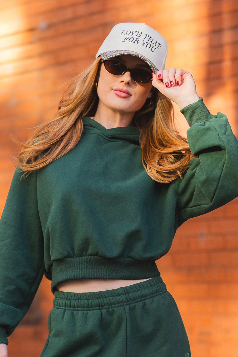 A person wearing sunglasses and a Love That For You Ivory & Leopard Two-Toned Trucker Hat with a leopard-print brim that says LOVE THAT FOR YOU.