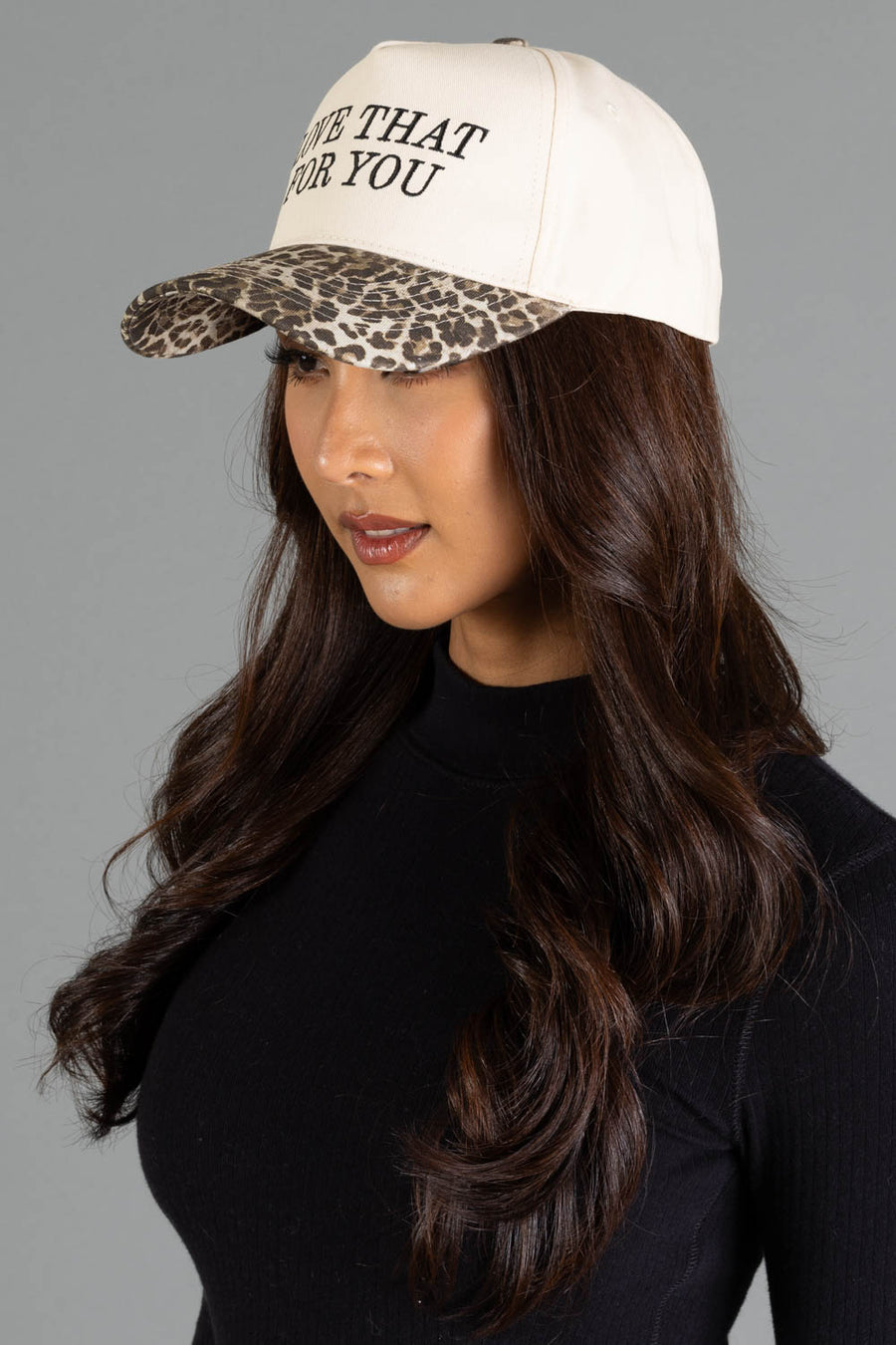 A person wears a Love That For You Ivory & Leopard Two-Toned Trucker Hat, featuring an ivory crown, leopard print brim, and the text LOVE THAT FOR YOU on the front.