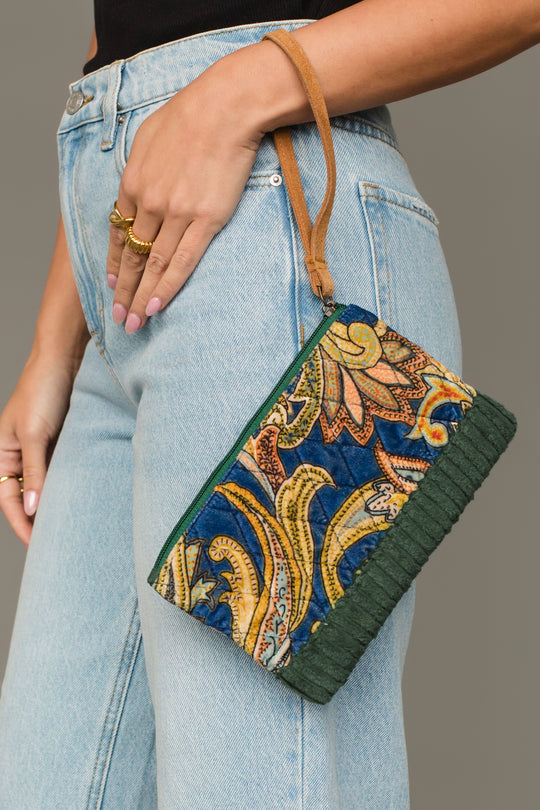 Woman carrying Panache Apparel Collection’s green and multicolored patterned wristlet with tan strap and textured trim.