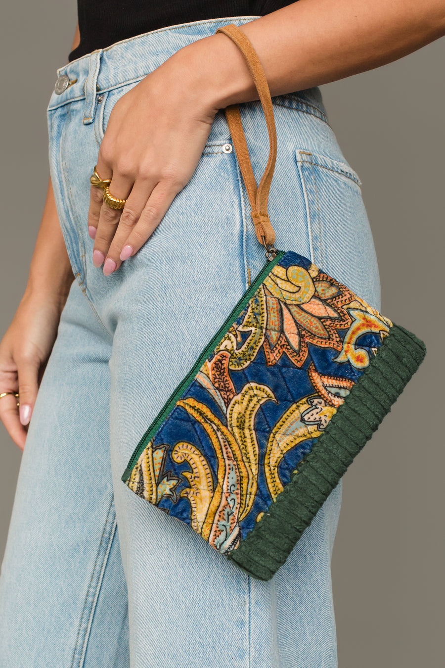 Woman carrying Panache Apparel Collection’s green and multicolored patterned wristlet with tan strap and textured trim.