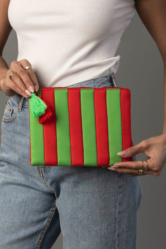 A person in a white tank top and blue jeans holds the Pink & Green Striped Clutch by Panache Apparel Collection.