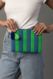A person wearing a white ribbed top and blue jeans holds the Blue & Green Striped Clutch from Panache Apparel Collection, featuring blue and green tassels.