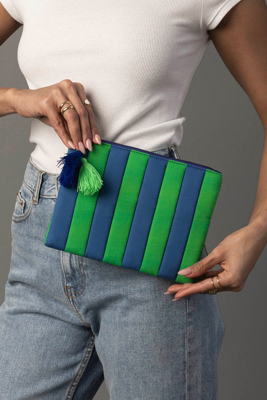A person in a white top and jeans holds the Panache Apparel Collection Blue & Green Striped Clutch, which features a green and blue tassel.