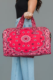 A person holds the Panache Apparel Collection Red Bandana Duffel by its handles, styled with light blue jeans and a black short-sleeved top, set against a plain gray background.