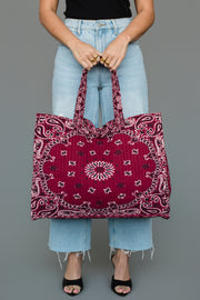 A person wearing light blue jeans and black heels holds the Panache Apparel Collection Burgundy Bandana Tote in front of a gray background.