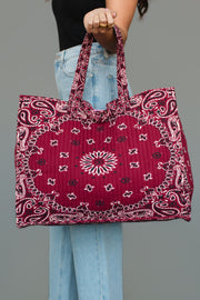 A person wearing light blue jeans and a black top holds the Panache Apparel Collection Burgundy Bandana Tote by its handles against a plain gray background.