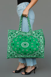 A person wearing light blue jeans and black heels holds the Panache Apparel Collection Green Bandana Tote by both handles.