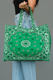 A person wearing light blue jeans and a black top holds the Green Bandana Tote by Panache Apparel Collection, featuring a large green design with a white bandana print, against a plain gray background.