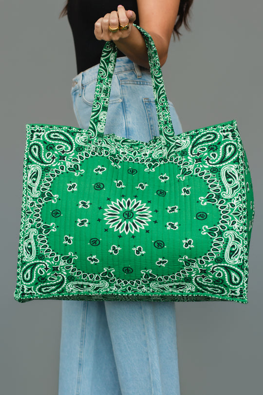 A person wearing light blue jeans and a black top holds the Green Bandana Tote by Panache Apparel Collection, featuring a large green design with a white bandana print, against a plain gray background.