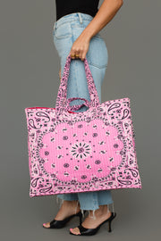 A person in light blue jeans and black heels holds the Panache Apparel Collection Pink Bandana Tote, featuring a paisley bandana pattern, against a plain gray background.