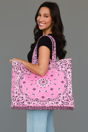A woman wearing a black shirt and jeans smiles while holding the Panache Apparel Collection Pink Bandana Tote, featuring a large size and paisley bandana pattern, against a plain gray background.