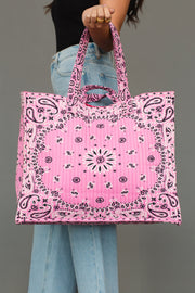 A person dressed in jeans and a black top holds the Pink Bandana Tote from Panache Apparel Collection, featuring a bold black and white paisley bandana pattern, set against a plain gray background.