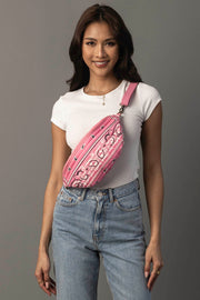 A woman wearing a white t-shirt and blue jeans smiles while posing with the Pink Bandana Crossbody from Panache Apparel Collection against a gray background.