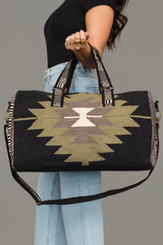 A person wearing a black top and light blue jeans holds the Panache Apparel Collection Black, Olive, Gray & Cream Western Duffel against a plain gray background.