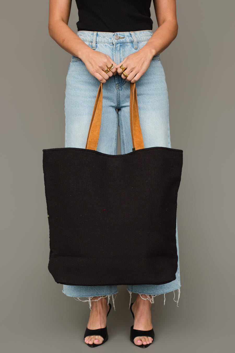 A person wearing a black sleeveless top, light blue jeans, and black heels holds the Panache Apparel Collection Black, Olive, Gray & Cream Western Tote in front of them against a plain background.
