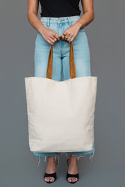 A person wearing a black top, light blue jeans, and black heels holds the Panache Apparel Collection Khaki, Gray & Tan Western Tote against a plain gray background.