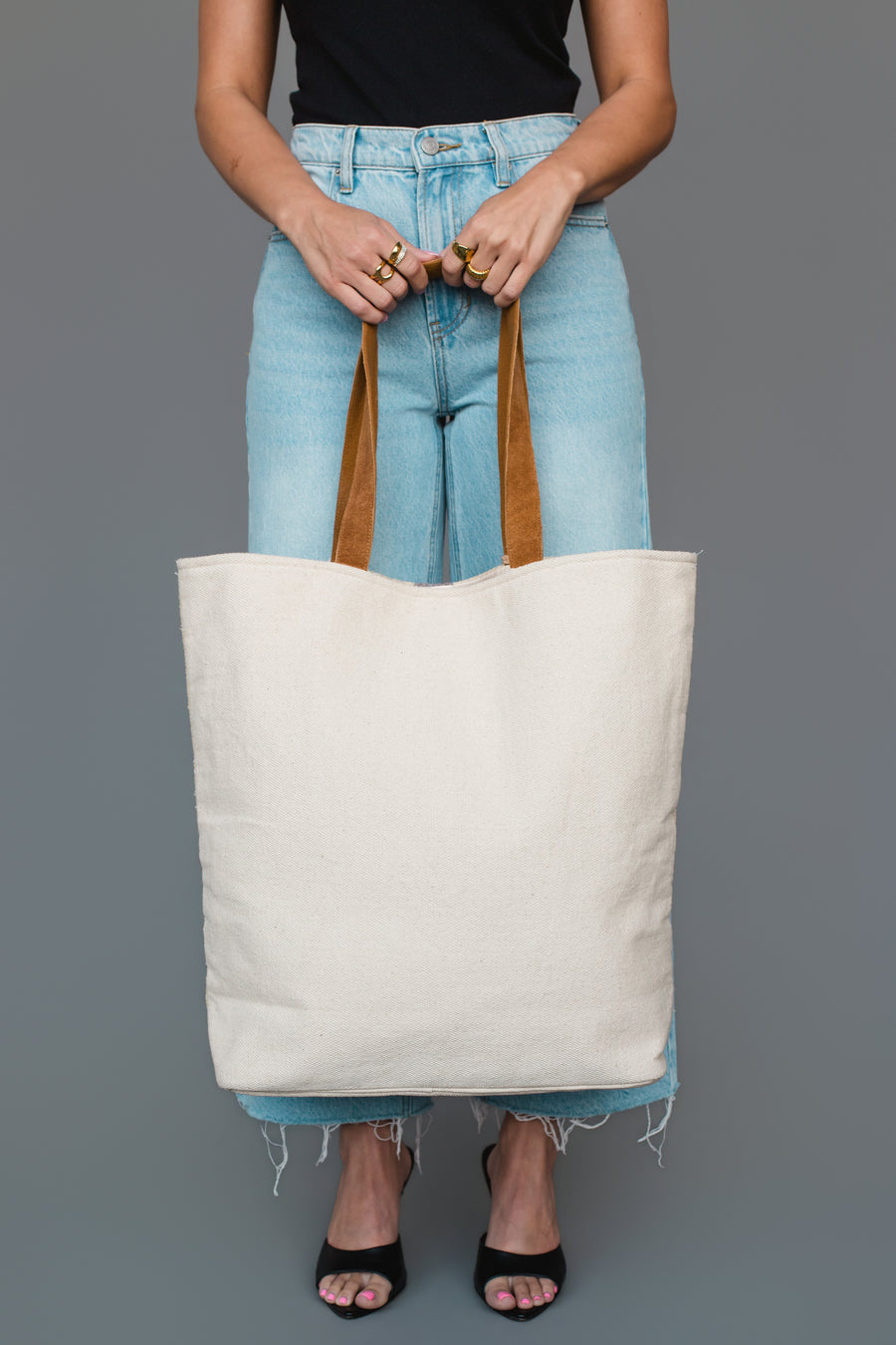 A person wearing a black top, light blue jeans, and black heels holds the Panache Apparel Collection Khaki, Gray & Tan Western Tote against a plain gray background.