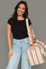 A woman with long brown hair, dressed in a black t-shirt and light blue jeans, smiles while holding the Panache Apparel Collection Cream, Brown & Rust Western Duffel over her shoulder. The background is plain gray.