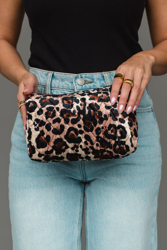 A person wearing a black top and light blue jeans holds the Panache Apparel Collection Brown & Cream Leopard Travel Pouch with both hands, displaying rings on their fingers.