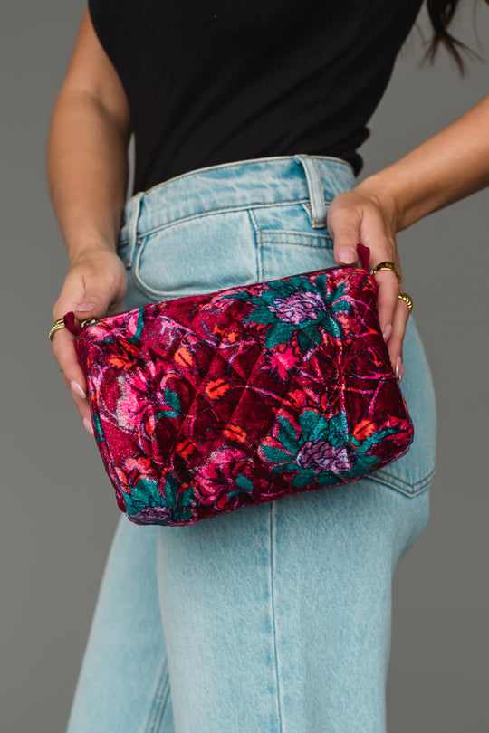 A person in a black top and light blue jeans holds the Panache Apparel Collection Burgundy & Multicolored Floral Wristlet with both hands.