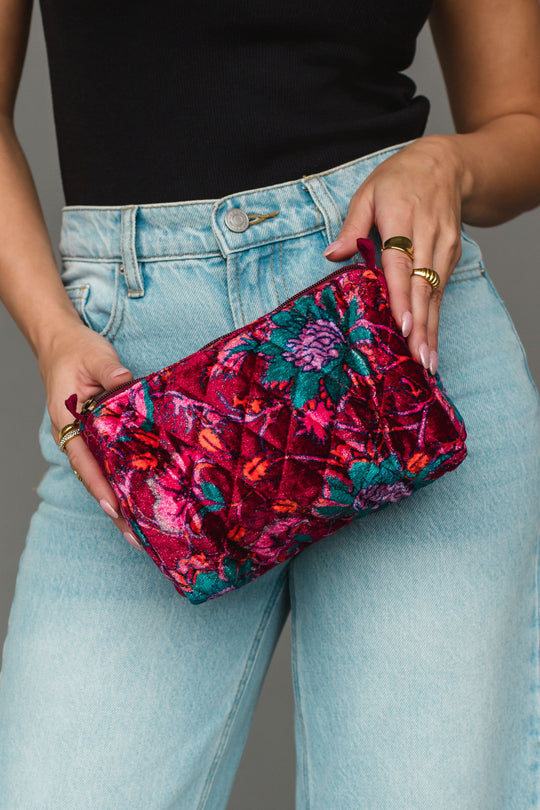 A person in light blue jeans and a black top holds the Burgundy & Multicolored Floral Wristlet by Panache Apparel Collection.