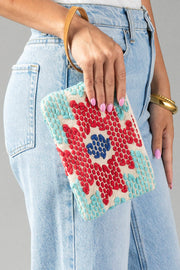 A person wearing blue jeans holds the Red, Turquoise & Blue Western Wristlet by Panache Apparel Collection, a small clutch featuring a vibrant geometric pattern in red, turquoise, and blue, complete with a tan strap.