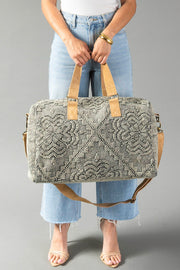 Wearing light jeans and a white top, a person holds the Panache Apparel Collection Gray Vintage Inspired Textured Duffel with tan handles and a detachable strap, standing against a plain gray background.