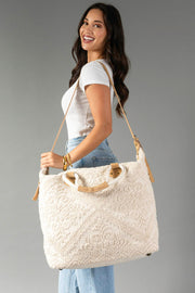 A smiling woman in a white t-shirt and jeans carries the Panache Apparel Collection’s Cream Vintage Inspired Textured Tote, featuring tan straps, while standing against a plain gray background.