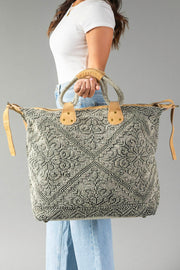 A woman in a white shirt and blue jeans holds the Gray Vintage Inspired Textured Tote by Panache Apparel Collection, featuring suede leather handles and a geometric design, against a plain gray background.