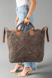 A person in jeans and heels holds the Panache Apparel Collection’s Brown Vintage Inspired Textured Tote, a large bag with short handles, side straps, an intricate woven pattern, and brown leather accents.