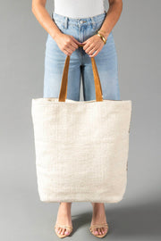 A model wearing light blue jeans and a white top holds the Panache Apparel Collection’s Cream, Brown & Rust Western Tote. Only the torso and legs are visible against a plain gray background.