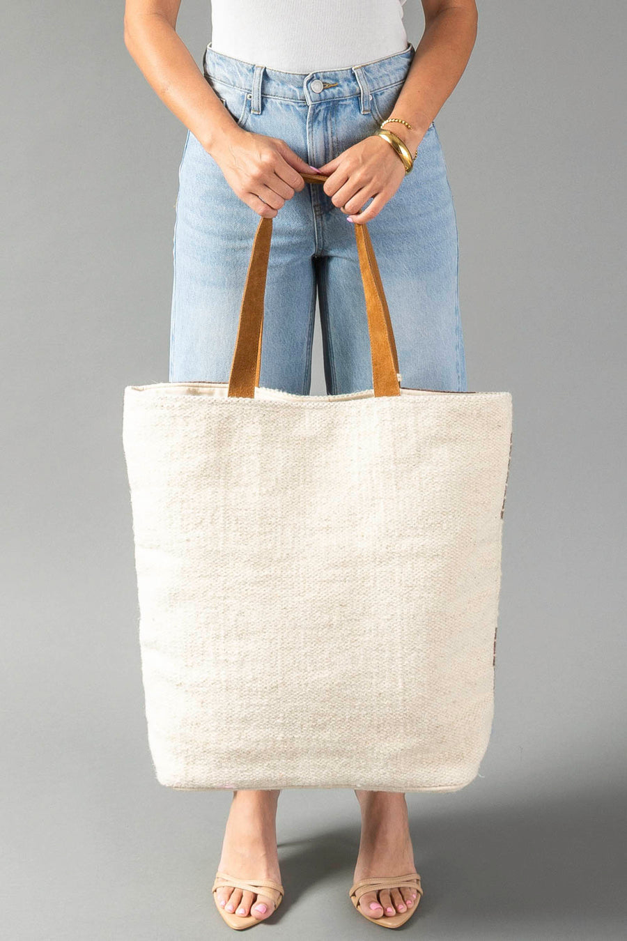 A model wearing light blue jeans and a white top holds the Panache Apparel Collection’s Cream, Brown & Rust Western Tote. Only the torso and legs are visible against a plain gray background.