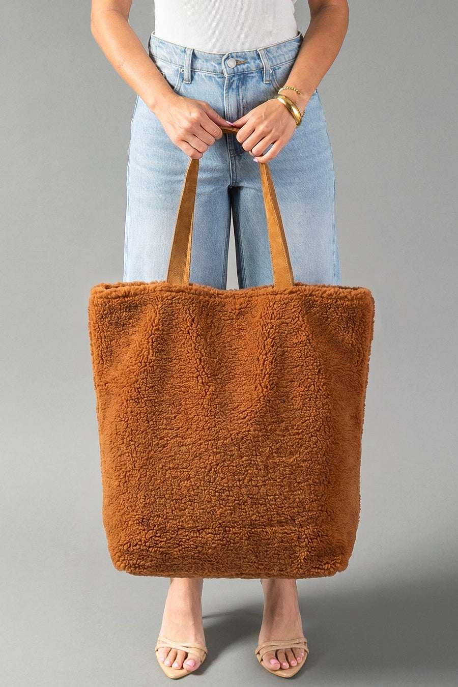 A person stands against a plain gray background holding the Panache Apparel Collection’s Orange, Cream & Pink Western Tote. They wear light blue jeans, a white top, sandals, and a gold bracelet.