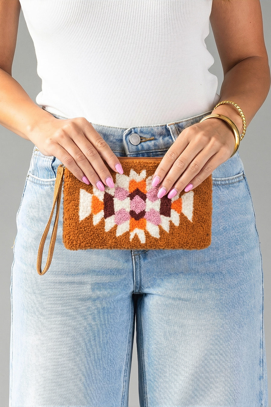 A person in a white tank top and light blue jeans holds the Panache Apparel Collection Orange, Cream & Pink Western Wristlet.