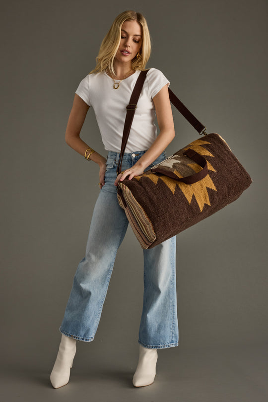 Woman holding a brown duffel bag with a sun design against a gray background