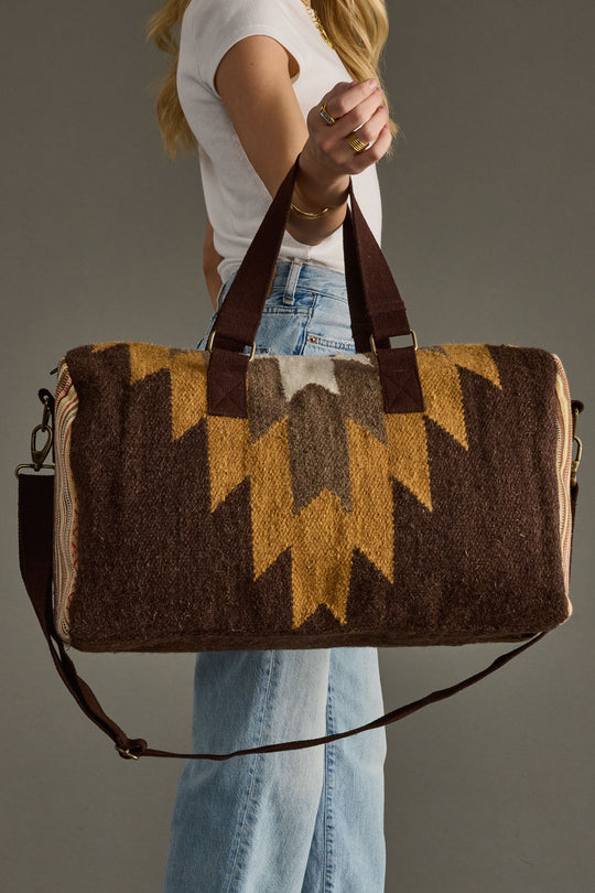 Person holding a patterned duffel bag against a neutral background