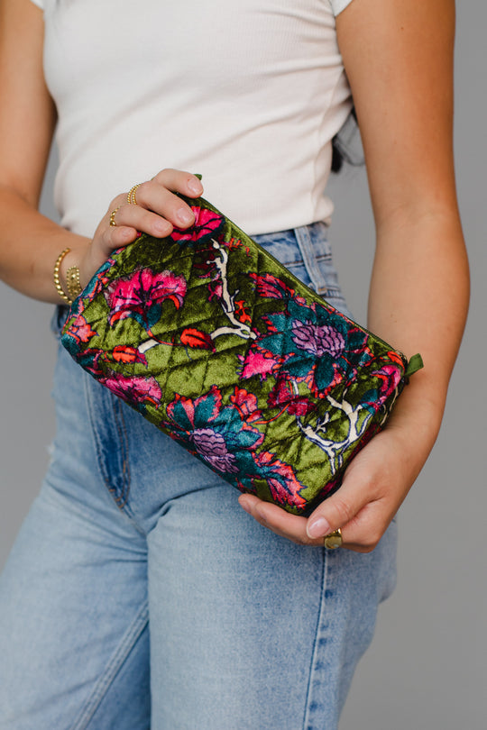 A person in a white sleeveless top and blue jeans holds the Panache Apparel Collection’s Dark Green & Multicolored Floral Travel Pouch, which features vibrant green, pink, purple, and red floral patterns and a convenient zipper closure.