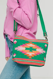 A person in a pink shirt and blue jeans carries the Panache Apparel Collection Green, Pink & Orange Western Crossbody, which features a colorful geometric pattern and an adjustable strap for comfort.